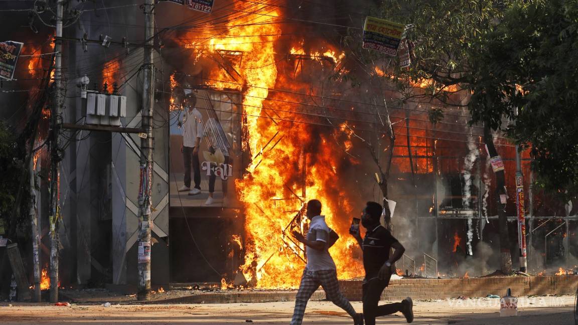 $!Los hombres corren frente a un centro comercial que fue incendiado durante una manifestación contra la Primera Ministra Sheikh Hasina.