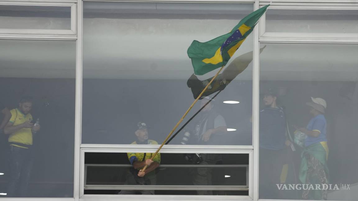 $!Un manifestante, partidario del expresidente brasileño Jair Bolsonaro, ondea una bandera brasileña desde una ventana tras asaltar el Palacio Planalto en Brasilia.