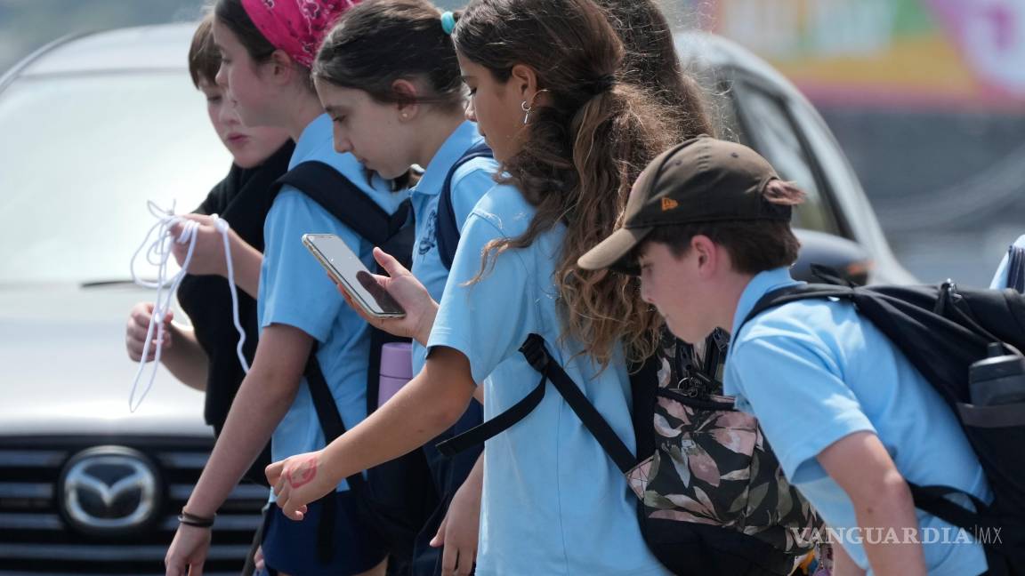 $!Una colegiala usa su teléfono mientras camina con un grupo de niños en Sídney, el lunes 8 de diciembre de 2025.