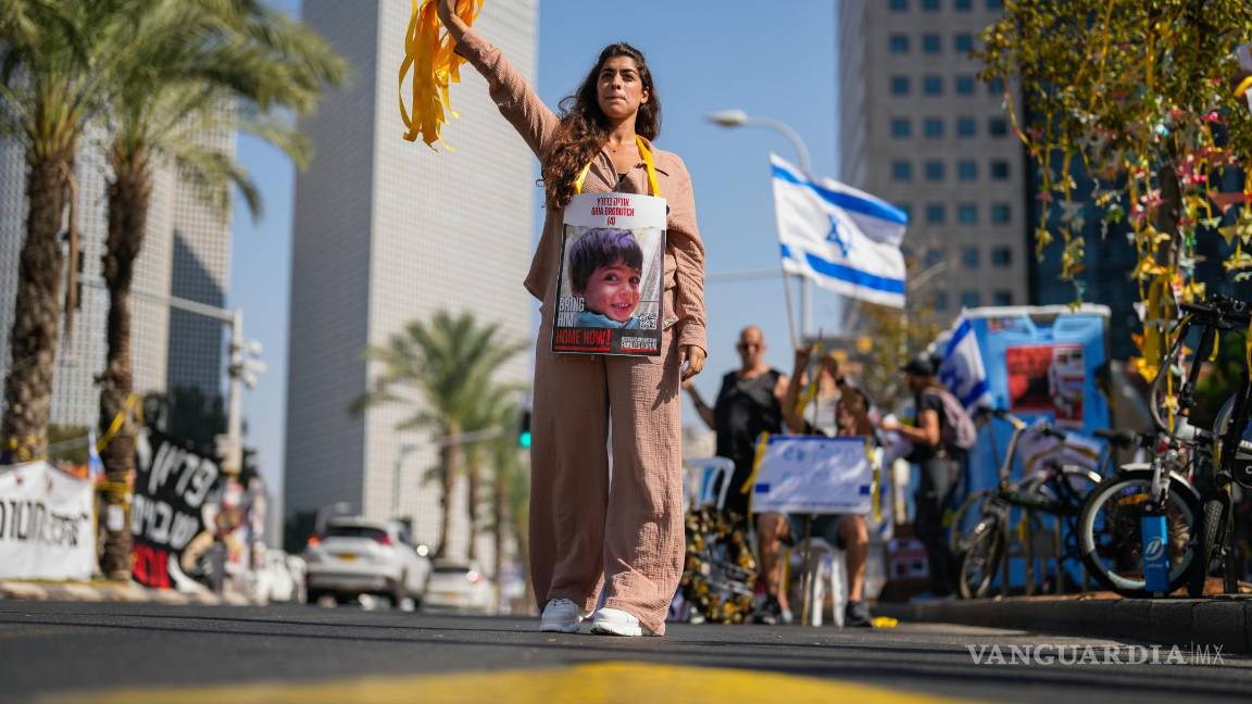 $!Una mujer, con la fotografía de un niño que es rehén de Hamás en Israel, entrega listones amarillos a los automovilistas en el centro de Tel Aviv, Israel.