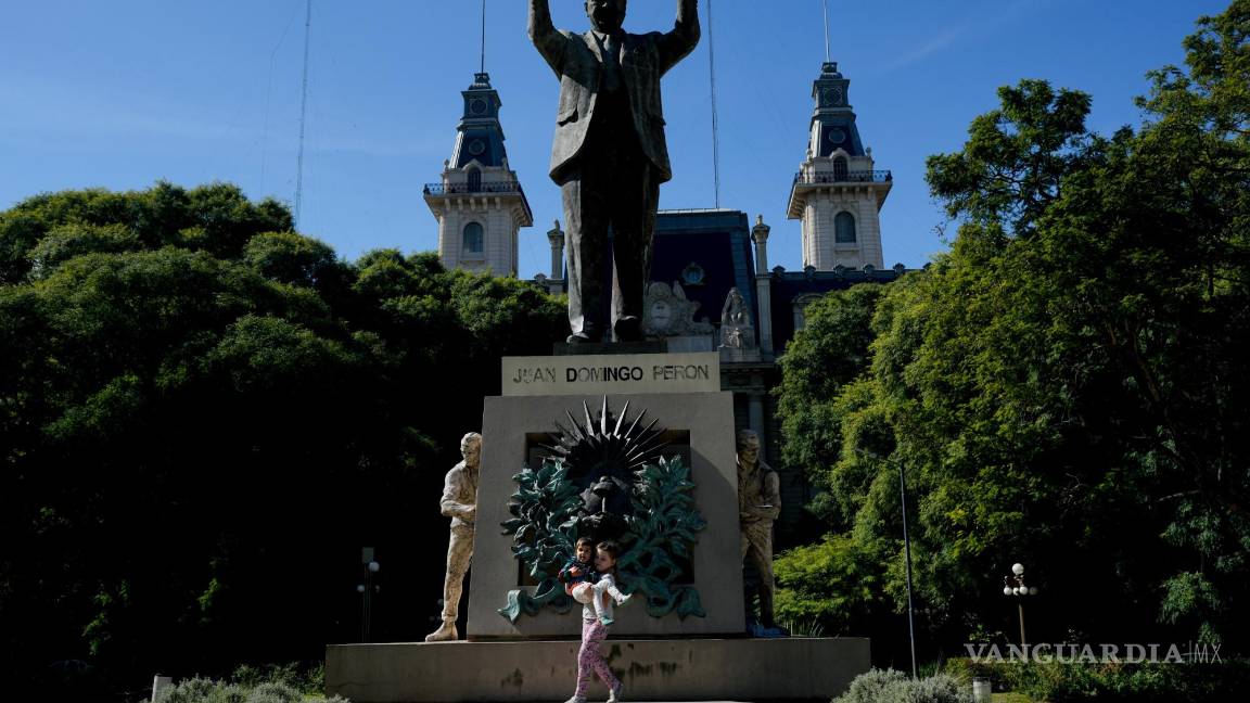 $!Aksinia Domini, de 6 años, carga a su hermanita Agata, de 3, frente a un monumento del expresidente argentino Juan Domingo Perón en Buenos Aires.