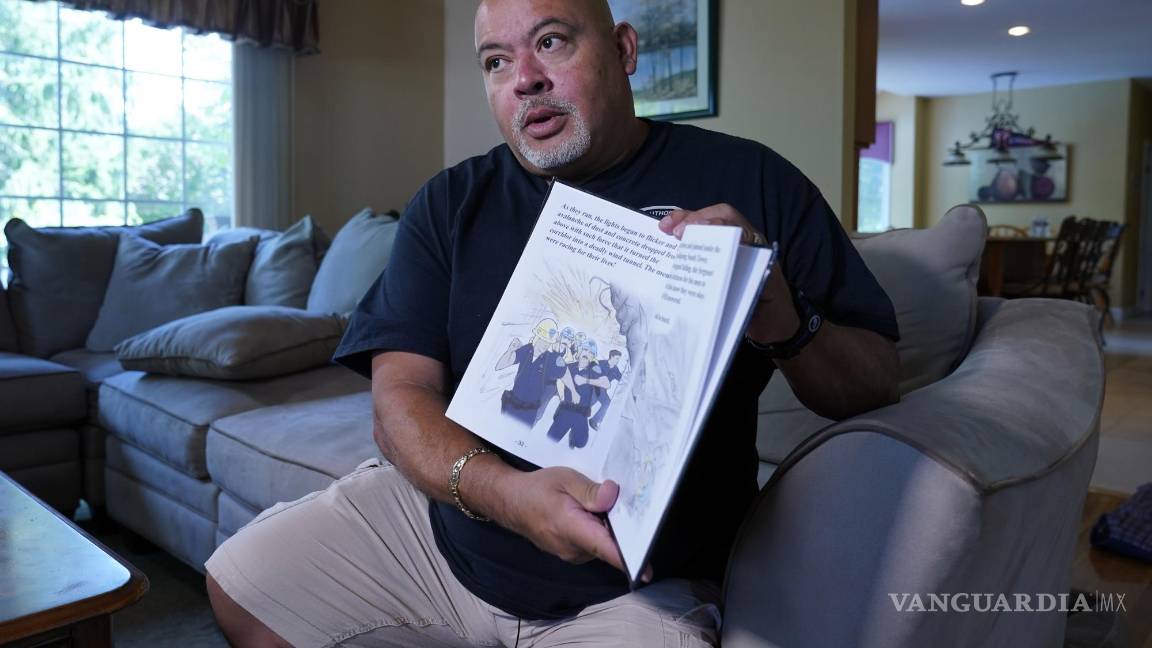 $!Will Jimeno, un ex agente de policía de la Autoridad Portuaria que, tras muchas horas, fue rescatado de entre los escombros del World Trader Center el 11S, sostiene el libro ilustrado para niños que escribió Immigrant, American, Survivor (“Inmigrante, Estadounidense, Sobreviviente”), en el que cuenta su experiencia, durante una entrevista en su casa es Chester, Nueva Jersey, el 2 de agosto de 2021. AP/Richard Drew