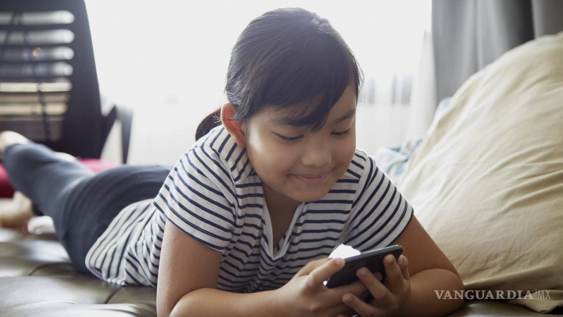 $!Niña sonriente utilizando su teléfono móvil en su cuarto.