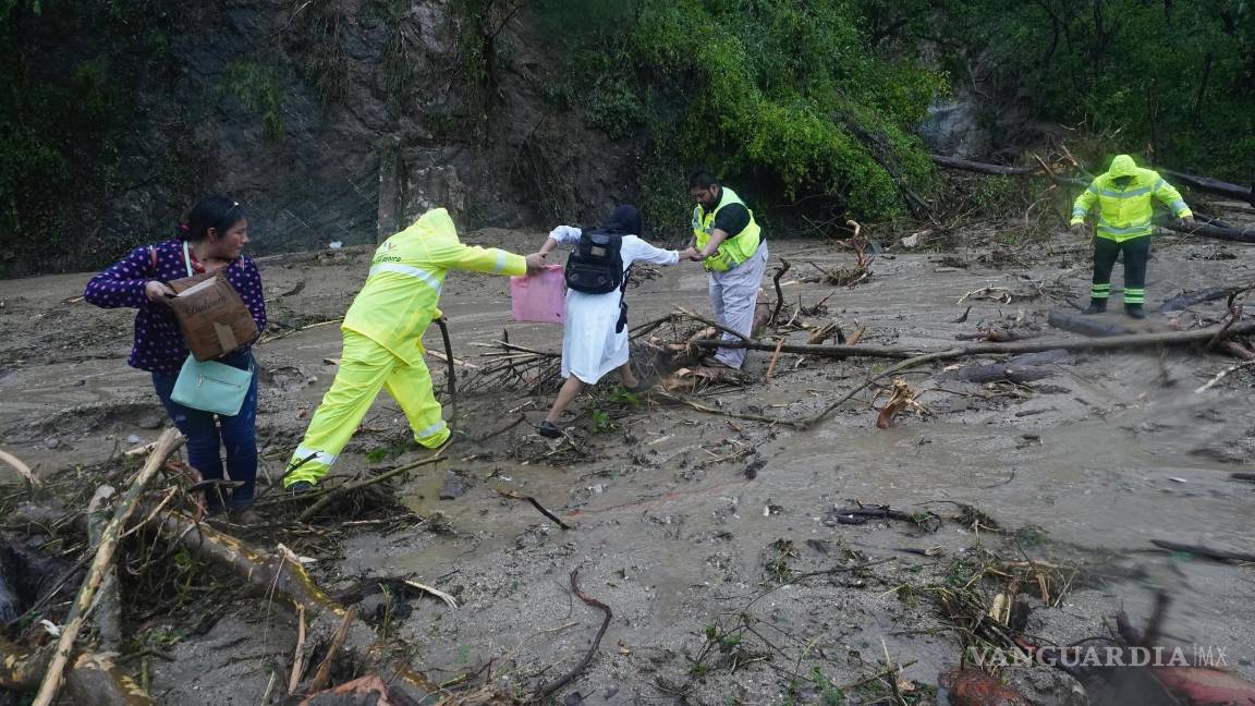 $!La gente recibe ayuda para cruzar una carretera bloqueada por un deslizamiento de tierra provocado por el huracán Otis cerca de Acapulco, México.