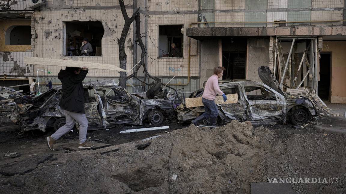 $!Gente carga tablones para cubrir las ventanas de un edificio dañado por una bomba el día anterior en Kiev, Ucrania.