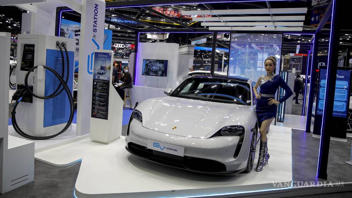 $!Un modelo se encuentra junto a un Porsche Cayman eléctrico en una estación de carga, en la 39.ª Exposición Internacional del Automóvil de Tailandia.