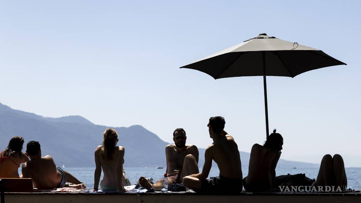 $!La gente descansa bajo una sombrilla en un cálido día de verano a orillas del lago de Ginebra, frente a las montañas de los Alpes suizos, en Vevey, Suiza.