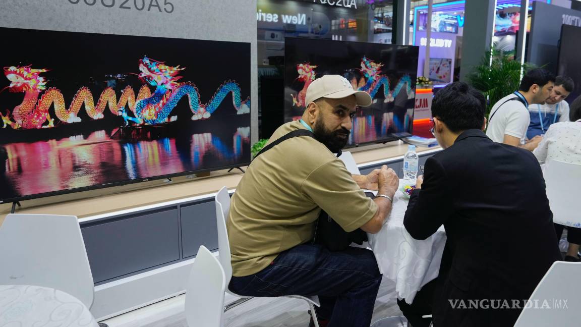 $!Visitantes se sientan cerca de televisores fabricados por Guangzhou HD Electronics Technology Co. Ltd., exhibidos en la Feria de Cantón en Guangzhou, China.