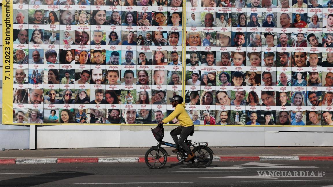 $!Una persona pasa en bicicleta junto a un cartel que muestra imágenes de rehenes israelíes retenidos por Hamás en Gaza, en Tel Aviv, Israel.