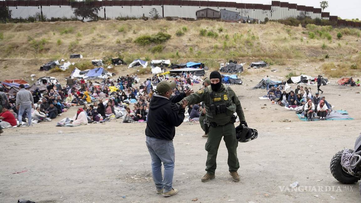 $!Un hombre bromea con un agente de la Patrulla Fronteriza mientras él y otros migrantes aguardan para solicitar asilo en San Diego.