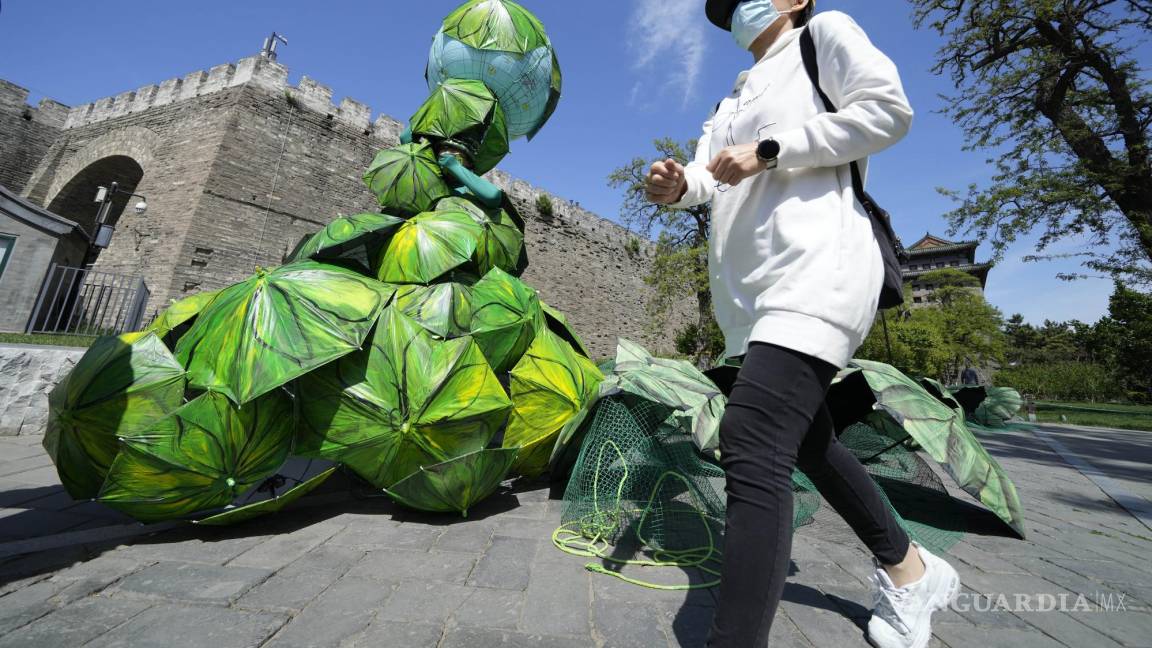 $!El artista chino Kong Ning con su último trabajo “Proteger la Tierra con sombrillas de hojas de plátano” para conmemorar el Día de la Tierra en Beijing.