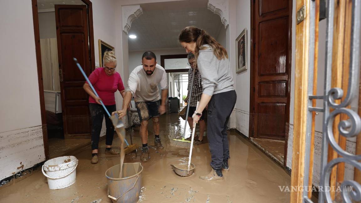 $!Varias personas limpian el lodo acumulado en el interior de su vivienda a causa de las intensas lluvias por la fuerte DANA en Valencia.