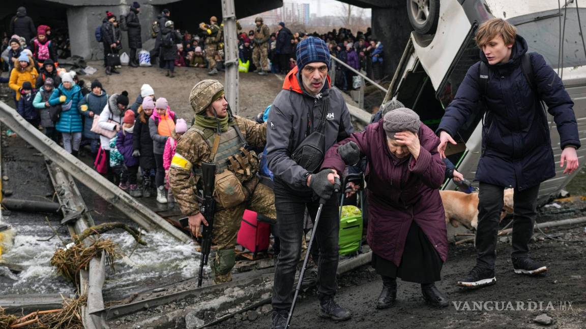 $!Una anciana es ayudada para cruzar el río Irpin por un paso improvisado bajo un puente destruido por las tropas ucranianas para ralentizar el avance ruso.