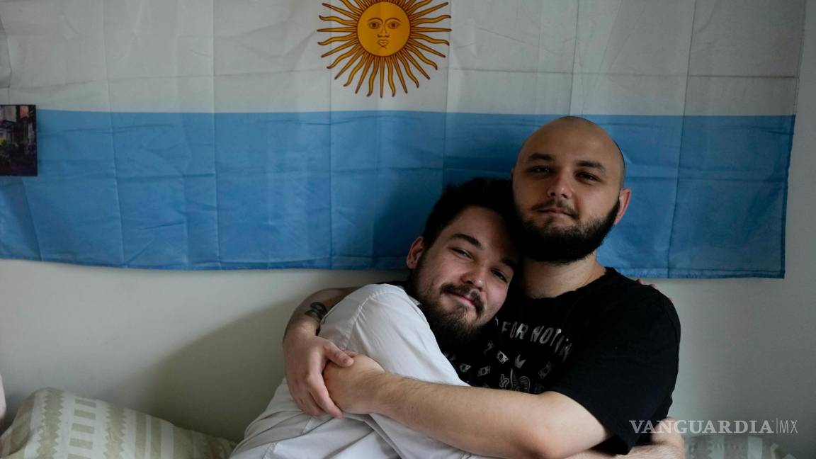 $!Los rusos Dmitri Yarin, a la izquierda, y su pareja Nikolai Shushpan, se abrazan frente a una bandera argentina en su casa en Buenos Aires, Argentina.