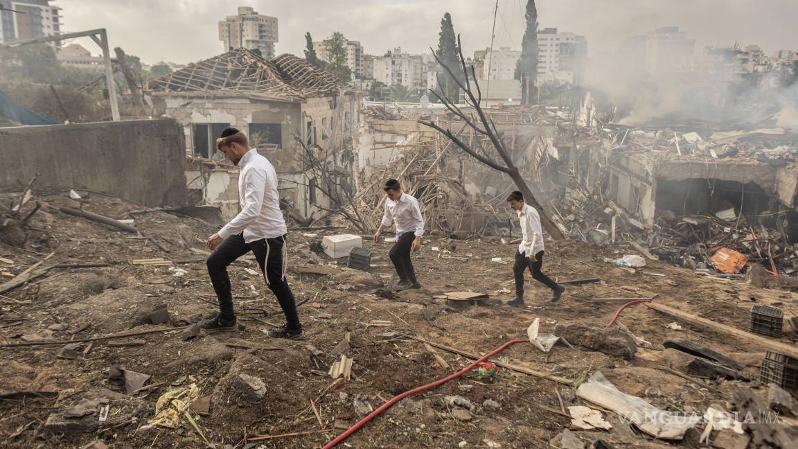 $!Personas caminando entre las ruinas de edificios dañados por un ataque con misiles iraníes en Rehovot, Israel.