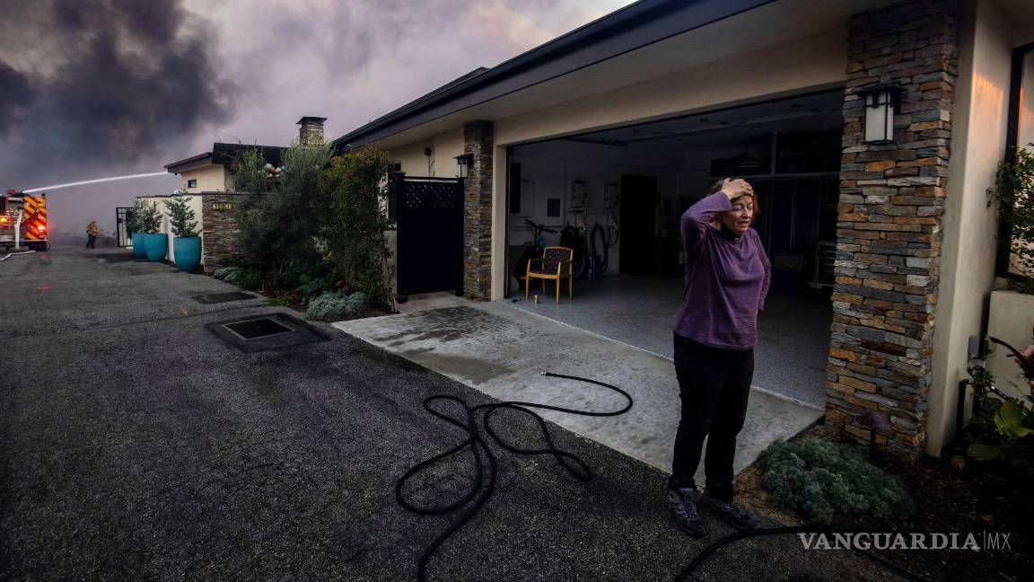 $!Una vecina se ve de pie delante de un garaje mientras los bomberos combaten el incendio de Palisades, en el vecindario de Pacific Palisades en Los Ángeles,.