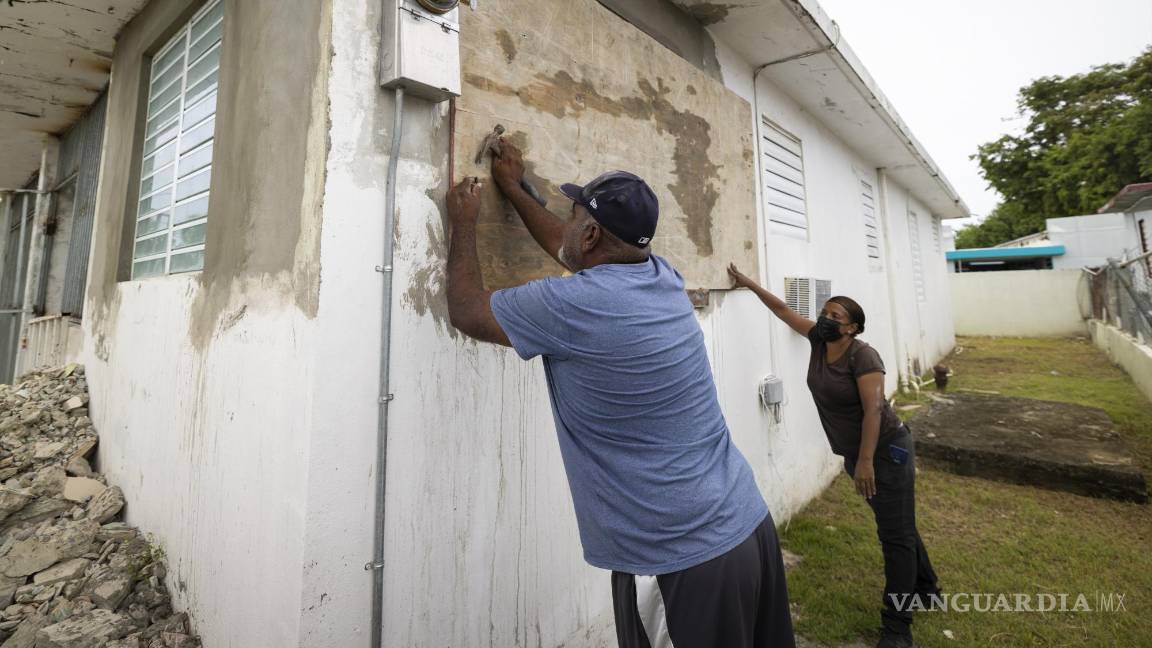 $!Residentes cubren una ventana de su casa ante la inminente llegada de la tormenta tropical Fiona.
