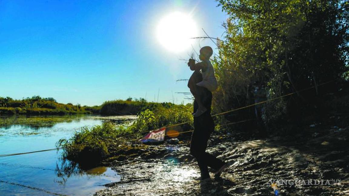 $!Al pie del Río Bravo, un migrante carga en sus hombros a un niño y ambos dirigen su mirada al otro lado del agua, hacia el anhelado sueño americano.