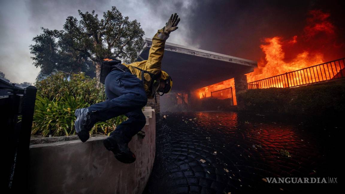 $!Un bombero salta una valla mientras lucha contra el incendio de Palisades en el barrio de Pacific Palisades de Los Ángeles.