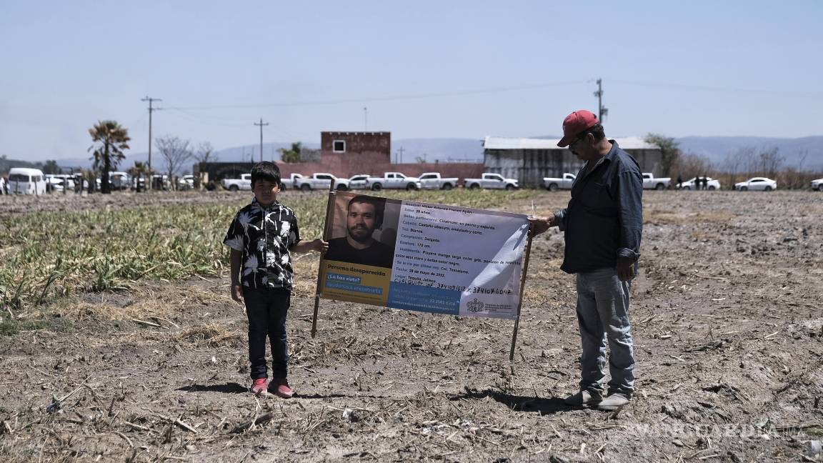 $!Dos personas sostienen una fotografía de un familiar desaparecido afuera del Rancho Izaguirre, donde se descubrieron restos óseos en Teuchitlán, Jalisco.