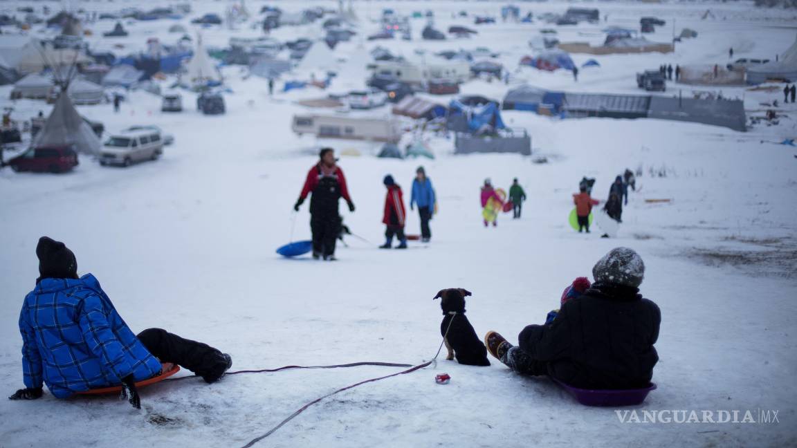 $!1/12/2016. Personas protestarncontra el oleoducto Dakota Access, al fondo mientras un niño se desliza en trineo por una colina en Cannon Ball, Dakota del Norte.