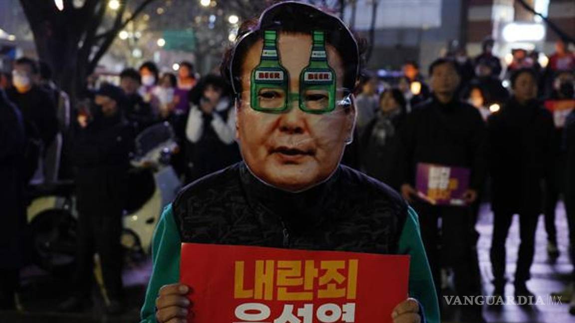 $!Un manifestante con una máscara que muestra el rostro del presidente Yoon Suk Yeol sostiene un cartel que dice: “¡Yoon Suk Yeol, dimite por traición!”.