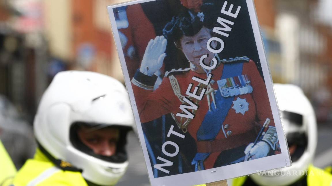 $!Un manifestante sostiene una pancarta con la imagen de la reina Isabel II frente a la policía en Dublín el 17 de mayo de 2011. AP/Tim Hales
