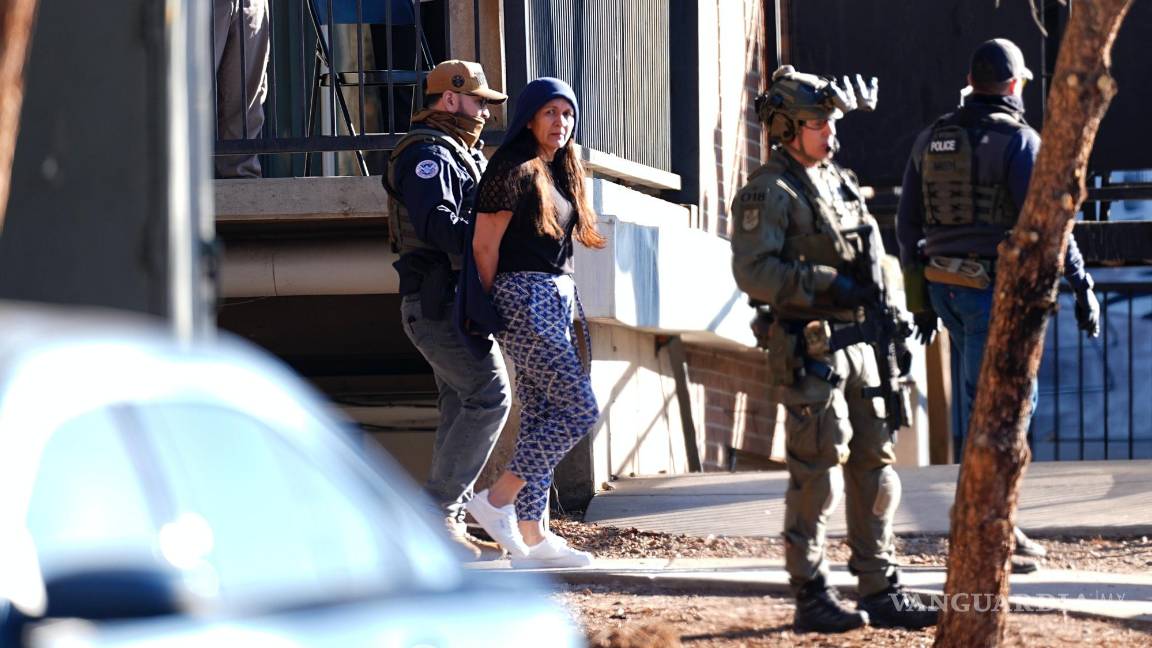 $!Mientras un vecino registra el momento con su teléfono, una mujer es sacada por autoridades de un departamento durante una redada en el este de Denver.