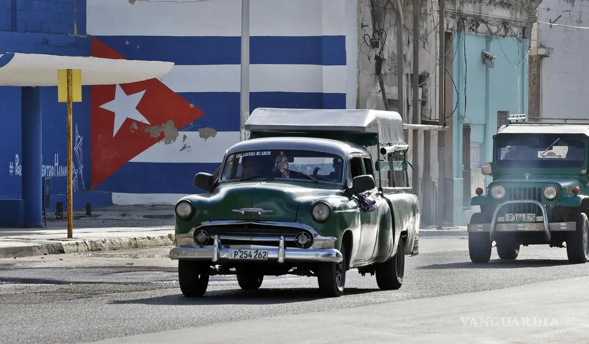 $!Vehículos antiguos transitan frente a un mural con la bandera de Cuba pintada, el 25 de octubre de 2026 en La Habana, Cuba.