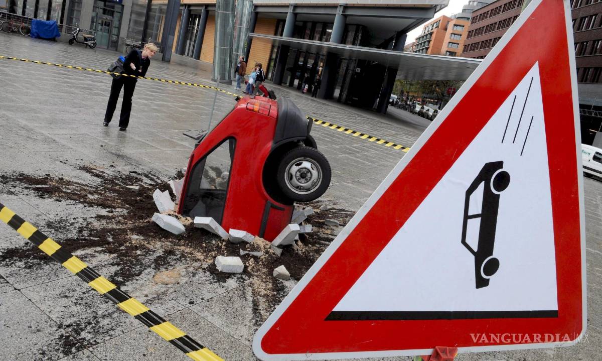 $!Unos peatones observan una escultura de un vehículo estrellado en la Postdam Square de Berlín. Los vídeos falsos cada vez abundan más.
