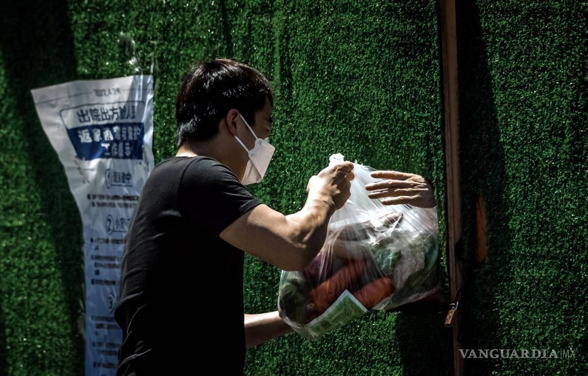 $!Un repartidor pasa comida a la persona en cuarentena a través del agujero en la cerca en medio del bloqueo de Covid-19 en curso en Shanghái, China.