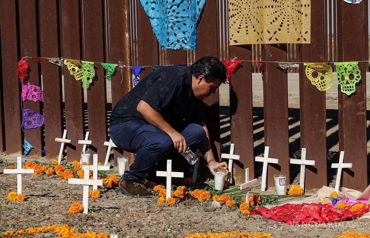 $!Un activista coloca una veladora en una ofrenda de Día de Muertos hoy, junto al muro fronterizo en Playas de Tijuana (México).