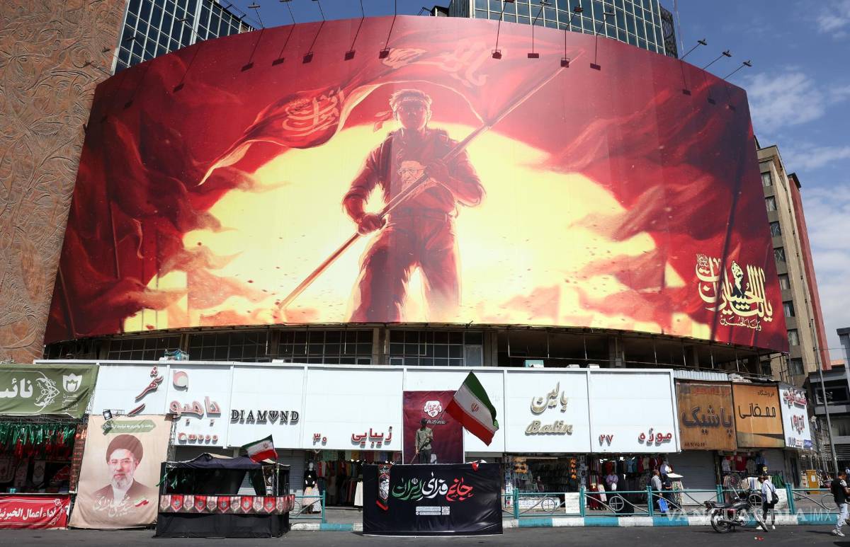 $!Un hombre iraní sostiene la bandera nacional de Irán frente a una gran valla publicitaria política en la plaza Valiasr de Teherán, Irán, el 1 de agosto de 2026.