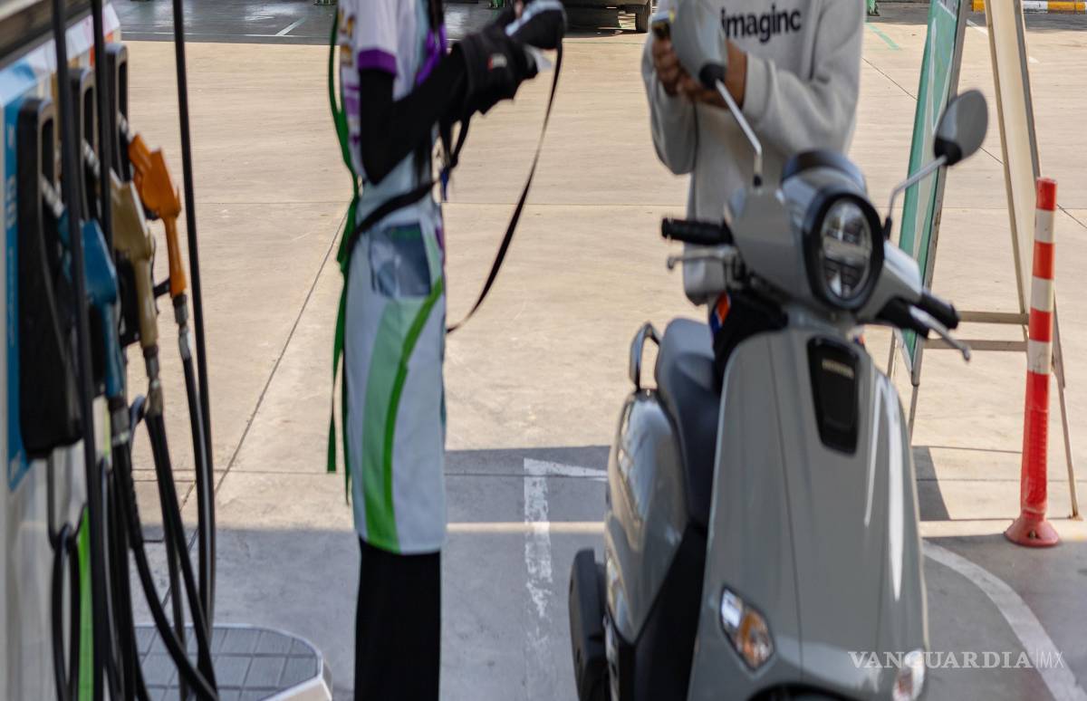 $!Un motociclista llena el tanque frente a un punto de recarga para vehículos eléctricos en una gasolinera en la provincia tailandesa de Nakorn Pathom.