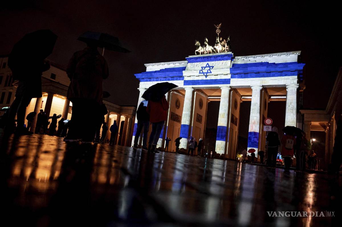 $!Personas observan la Puerta de Brandenburgo se ilumina con los colores de la bandera israelí como muestra de solidaridad, en Berlín, Alemania.