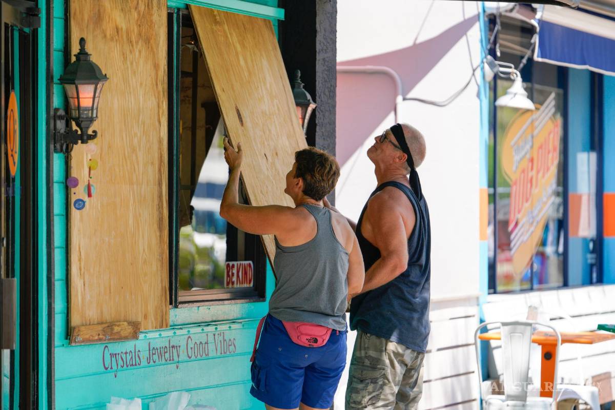 $!Lisa Bromfield y Mike Sernett colocan una hoja de madera en las ventanas delanteras de una tienda en el centro de Gulfport.