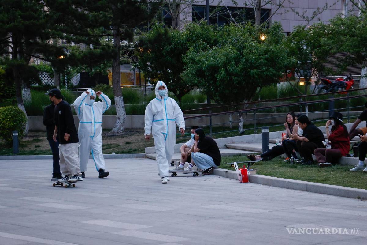 $!Los trabajadores de la salud con trajes protectores pasan junto a los patinadores que pasan el rato a lo largo de un río en Beijing, China.