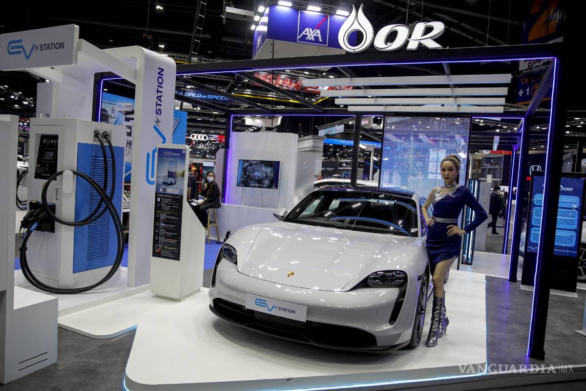 $!Un modelo se encuentra junto a un Porsche Cayman eléctrico en una estación de carga, en la 39.ª Exposición Internacional del Automóvil de Tailandia.