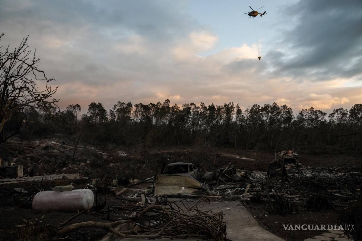 $!Un helicóptero arroja agua sobre puntos calientes cerca de casas quemadas en Kula, Hawái.