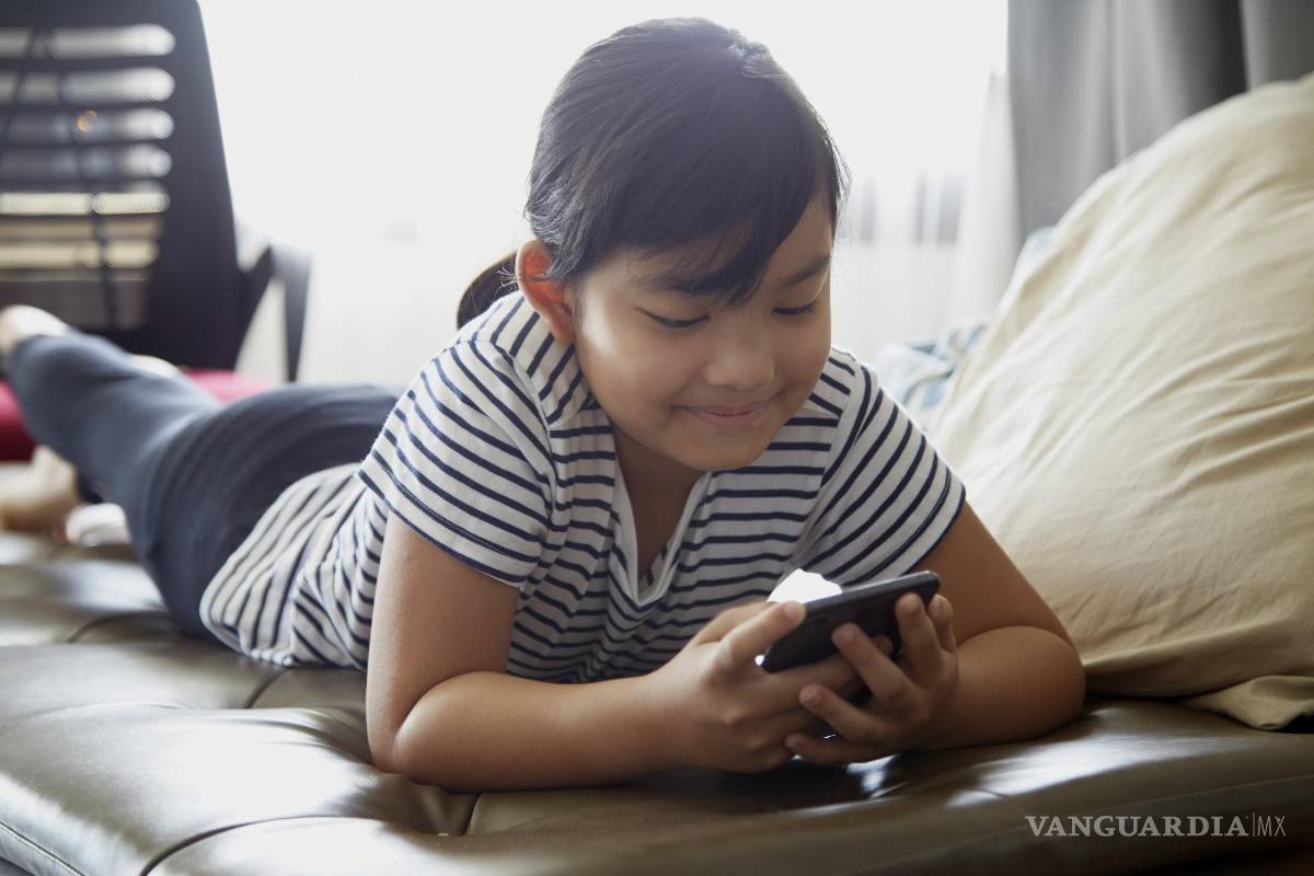 $!Niña sonriente utilizando su teléfono móvil en su cuarto.