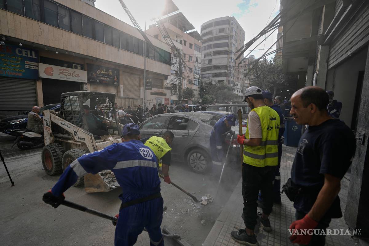 $!Trabajadores municipales limpian los escombros de una calle junto a un edificio residencial dañado en el ataque aéreo israelí en el suburbio sur de Hareit Hreik.