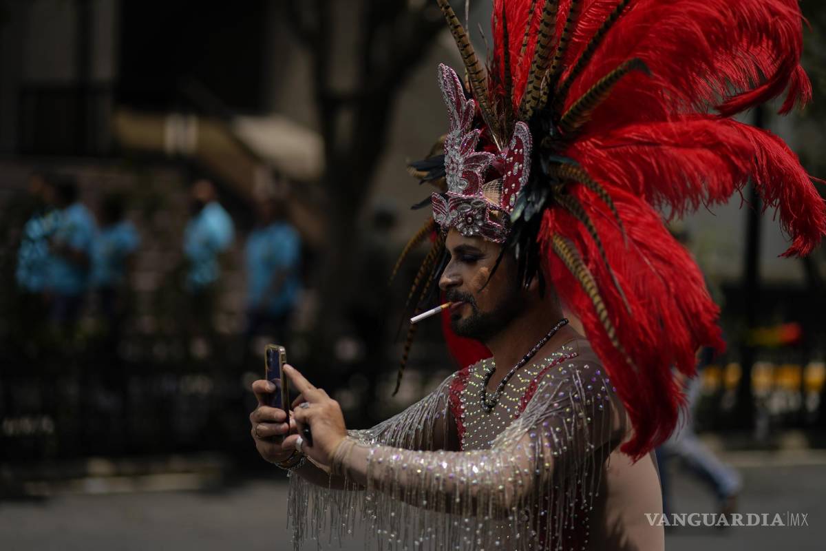 $!Un participante, con un tocado azteca y fumando un cigarrillo, posa para una selfie mientras participa en la marcha anual del Orgullo en la Ciudad de México.