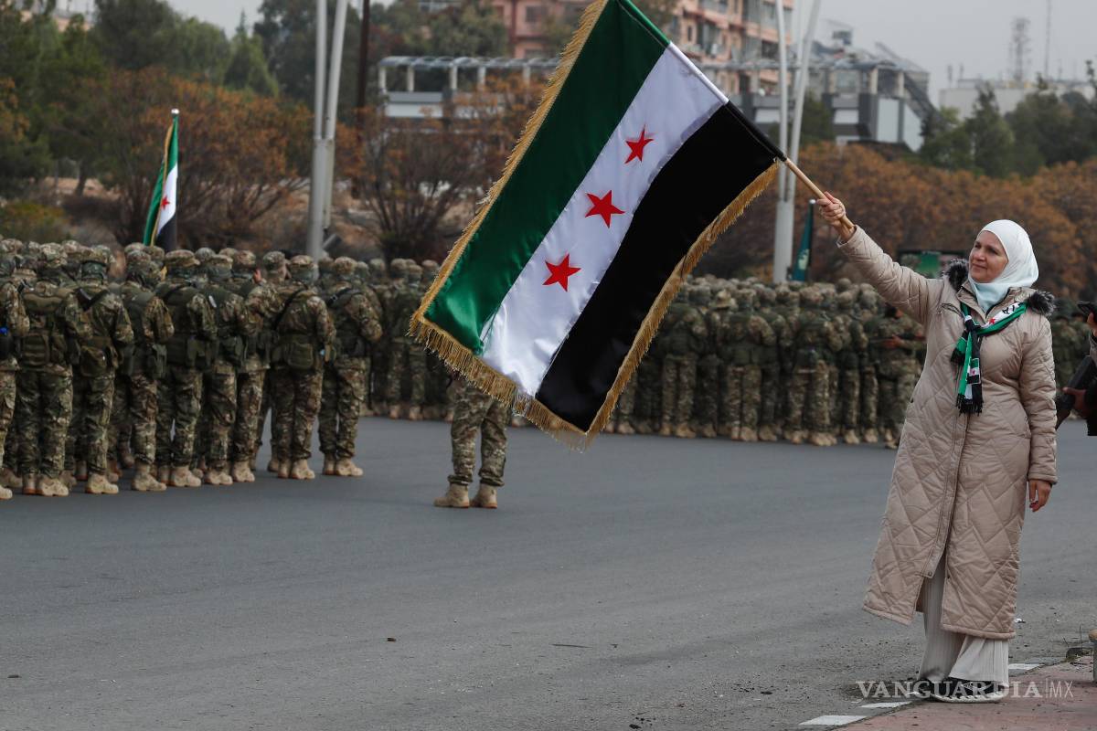 $!Una mujer y miembros del nuevo ejército sirio se forman antes del desfile militar por las celebraciones del año del derrocamiento del expresidente Bashar al-Assad