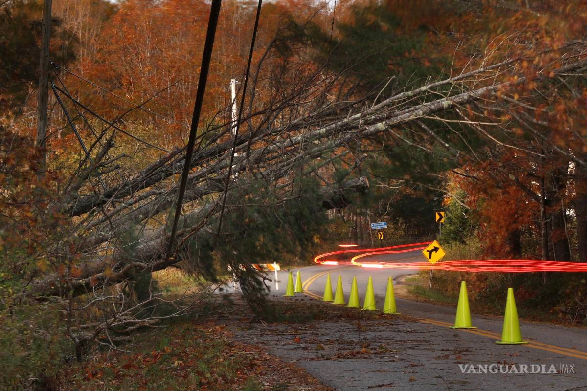 $!Un automóvil deja un rastro de luz al pasar por debajo de las líneas eléctricas afectadas por los árboles derribados en Freeport, Maine.