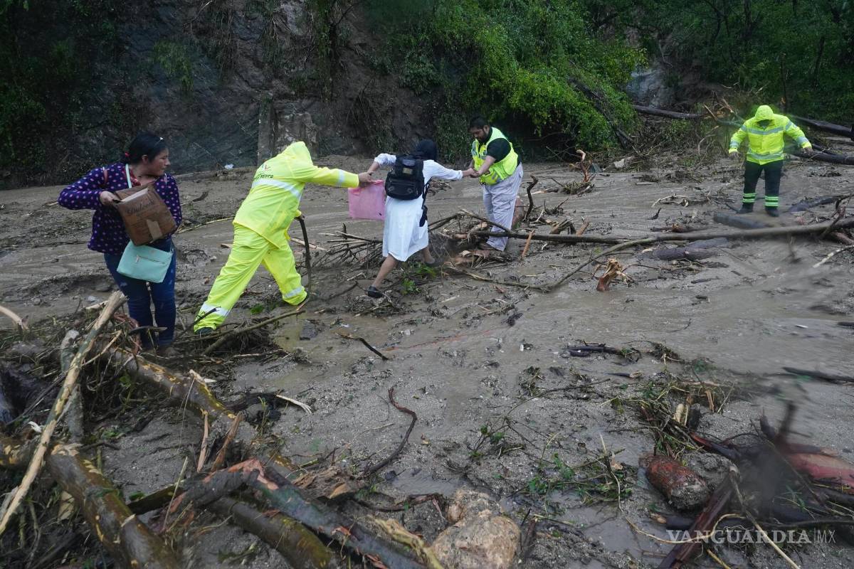 $!La gente recibe ayuda para cruzar una carretera bloqueada por un deslizamiento de tierra provocado por el huracán Otis cerca de Acapulco, México.