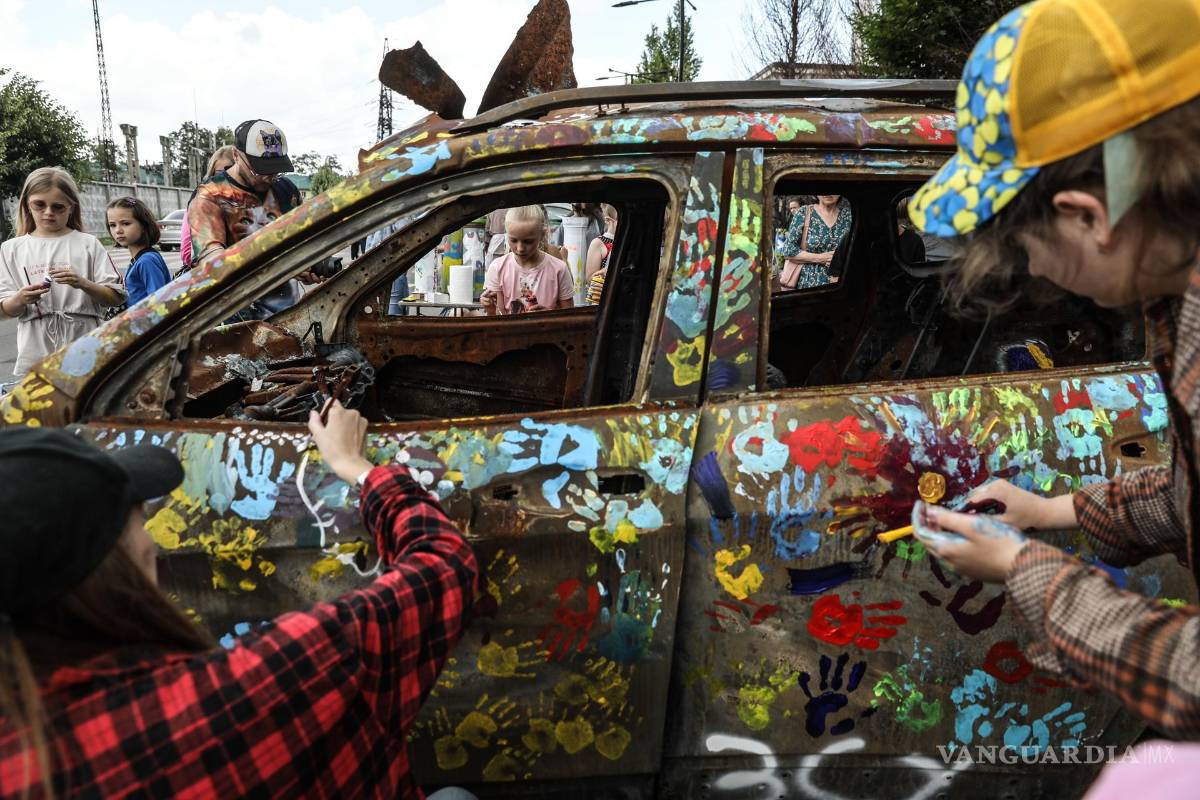 $!Artistas pintan junto a un grupo de niños coches quemados durante los combates entre las tropas ucranianas y rusas, este viernes en Bucha, Ucrania.