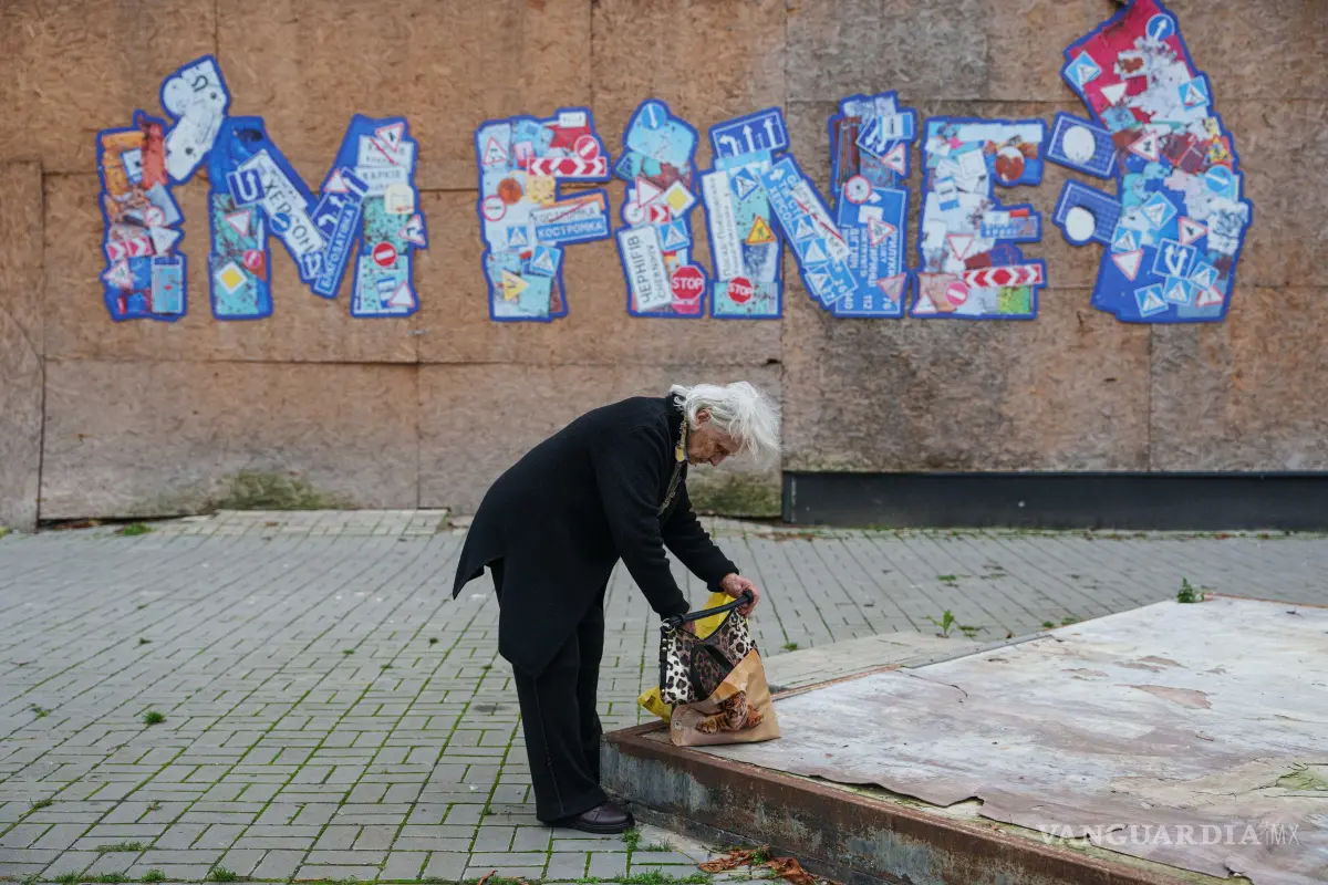 $!Una mujer mira dentro de su bolso frente a un grafiti que dice “Estoy bien”, durante un alto el fuego local para evacuar a los residentes de Oleshky, en Jersón, Ucrania.