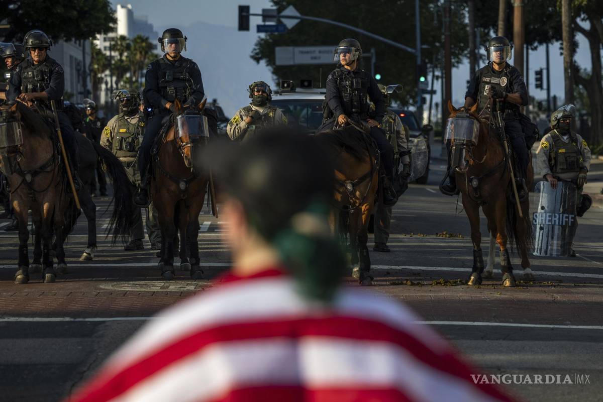 $!Agentes de policía, frente a manifestantes en el exterior del edificio del ayuntamiento durante protestas contra las redadas migratorias federales en Los Ángeles.