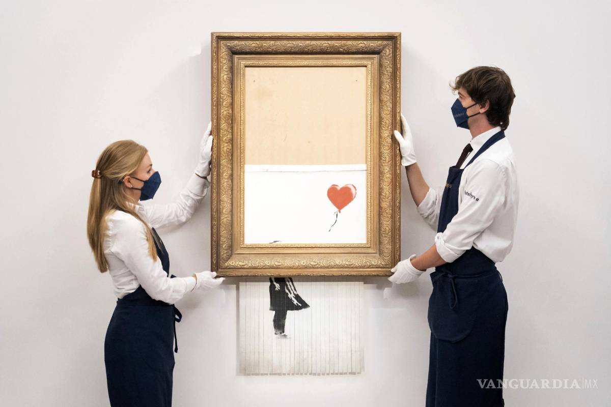 $!En esta foto del 3 de septiembre de 2021, manipuladores de arte sostienen Love is in the Bin de Banksy en la casa de subastas Sotheby's en Londres. AP/Dominic Lipinski/PA