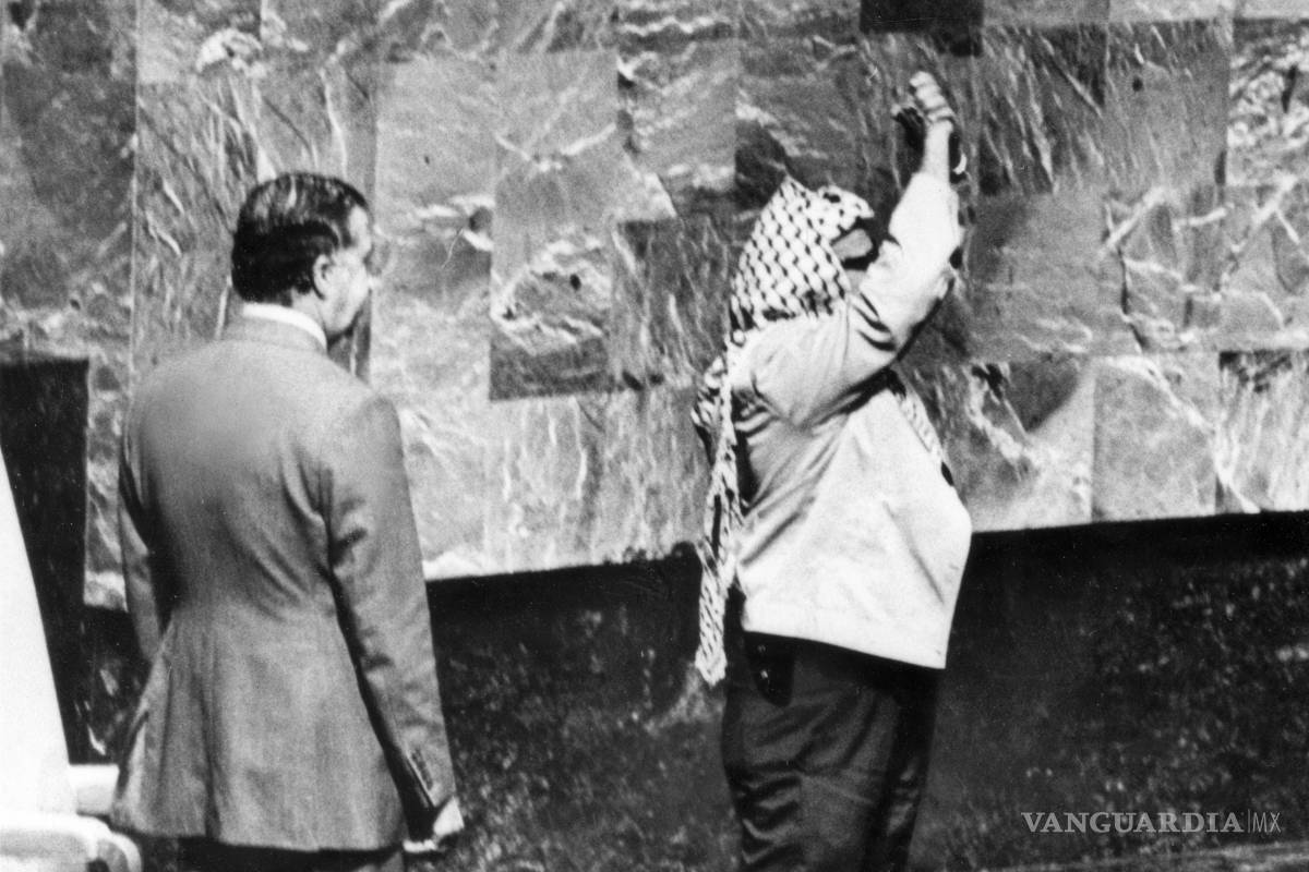 $!Una funda de pistola sobresale debajo de la chaqueta de Yasser Arafat mientras junta las manos sobre su cabeza en su aparición ante la Asamblea General de Naciones Unidas en la sede del organismo, el 13 de noviembre de 1974.